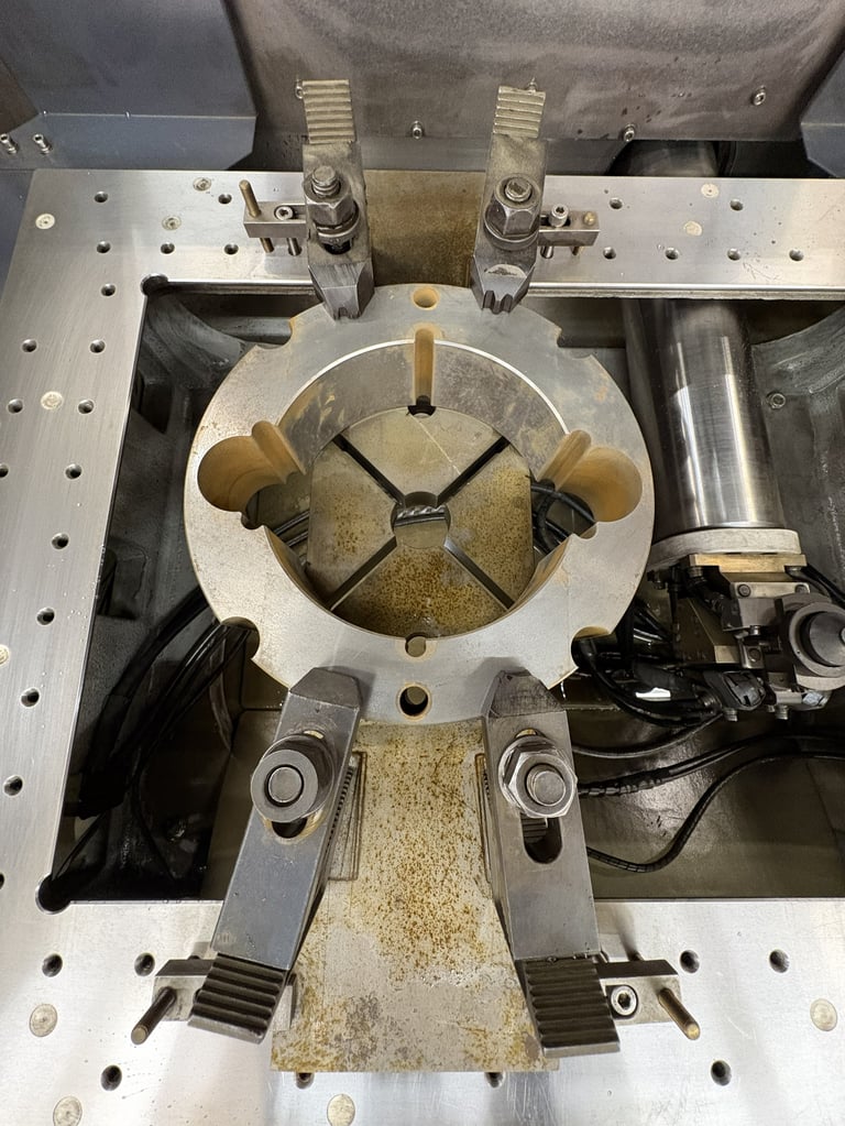 Top view of industrial machinery with circular metal chuck holding sample or workpiece, mounted on aluminum base plate with mechanical clamps