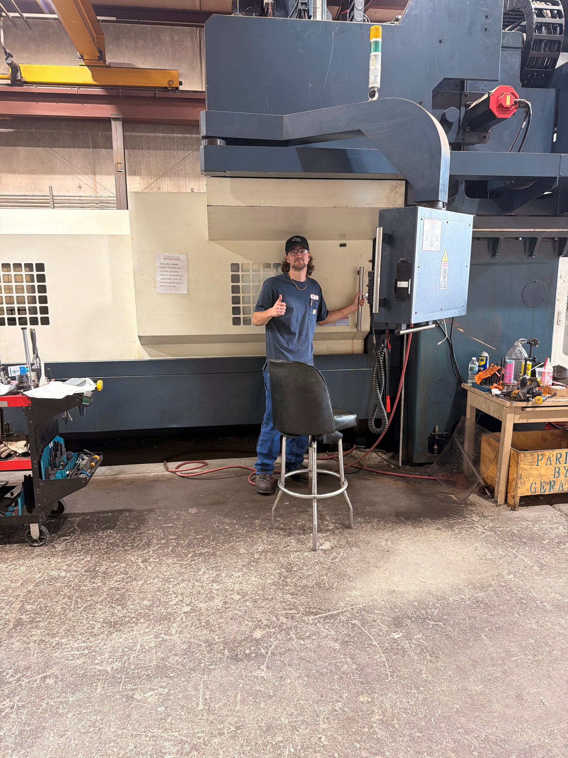 Worker standing in front of large industrial CNC machining center in a factory workshop