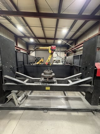 Industrial robotic arm mounted in metal enclosure with steel framework and work platform inside factory warehouse