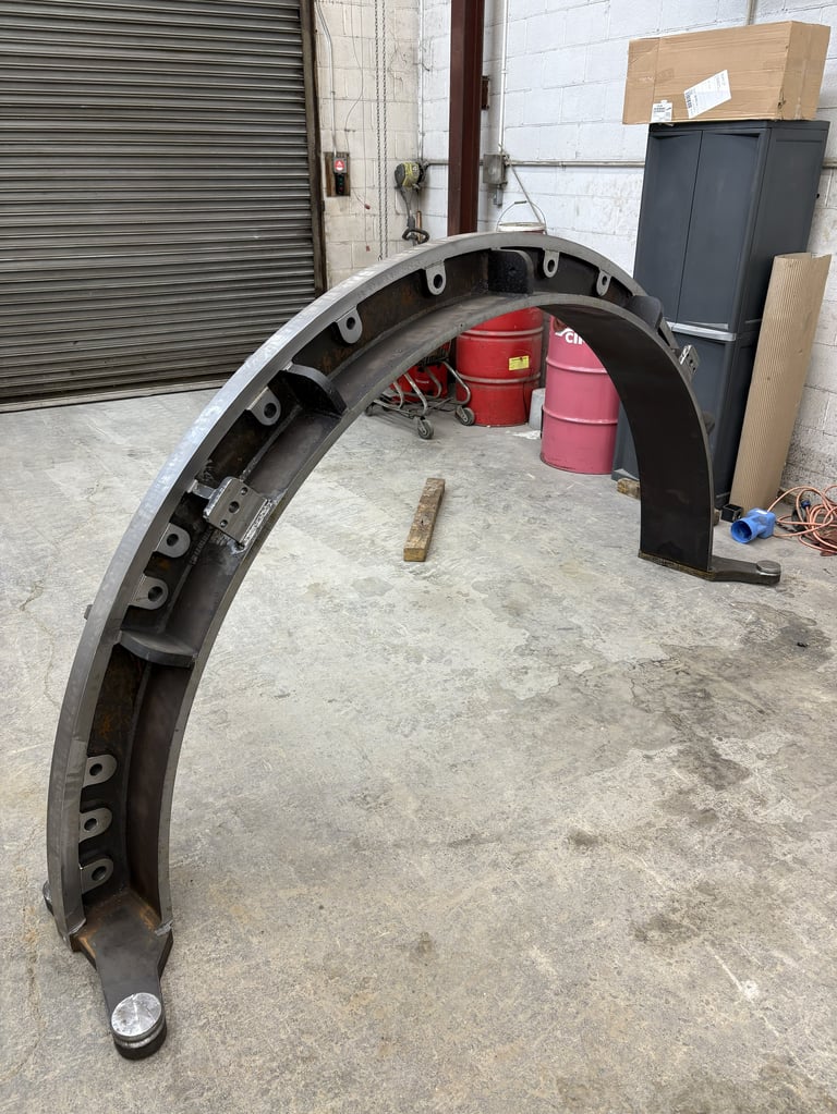 Black curved vehicle fender or trim piece lying on concrete floor in industrial warehouse setting with red drums and equipment in background